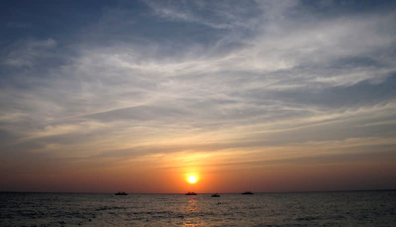 FILE PHOTO: The sun sets behind boats anchored off Seven Mile Beach in George Town, Cayman Islands