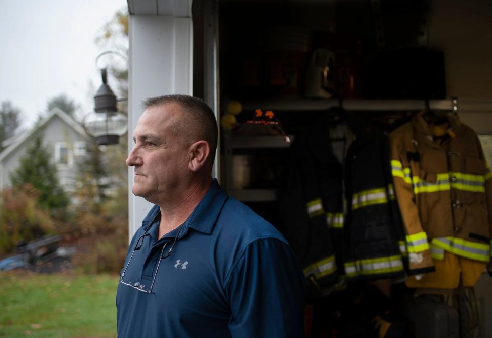 Former Worcester Firefighter Lt. Paul Cotter with turnout gear behind him Oct. 26, 2021, in Rindge, N.H.. Cotter and his wife Diane previously stored the gear in protective plastic in the garage. They took it out for the photo.
