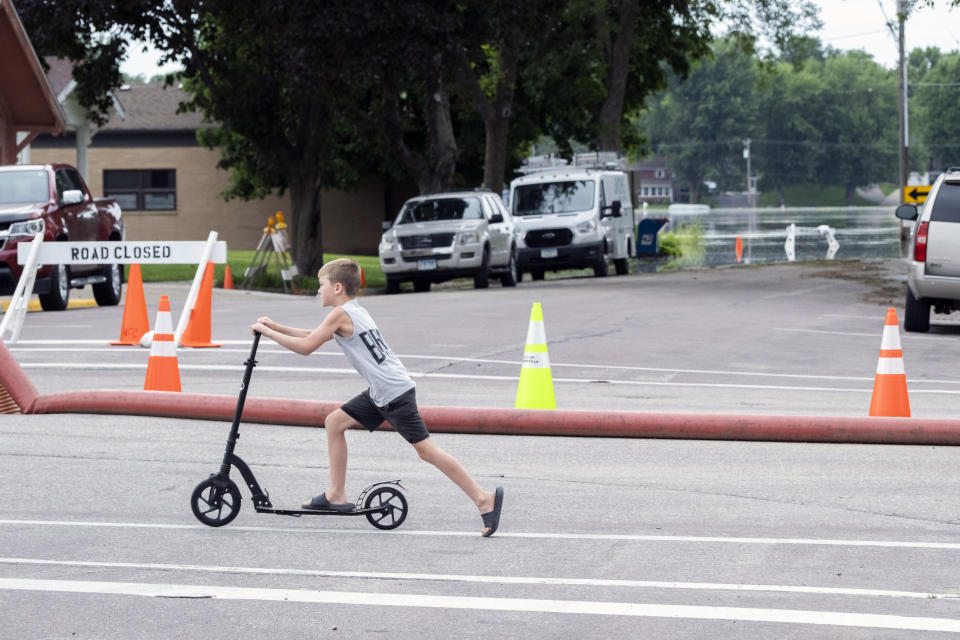 Kason Fisher wheels past flood waters from Sakatah Lake in downtown Waterville, Minn., on Tuesday, June 25, 2024. (Casey Ek/The Free Press via AP)