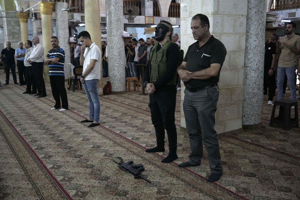 A masked gunman prays during the funeral for Palestinians killed during an Israeli military raid in the occupied West Bank town of Jenin, Wednesday, Sept. 28, 2022. At least four Palestinians were killed and dozens of others wounded, the Palestinian Health Ministry reported, the latest in a series of deadly Israeli operations in the occupied territory. (AP Photo/ Majdi Mohammed)