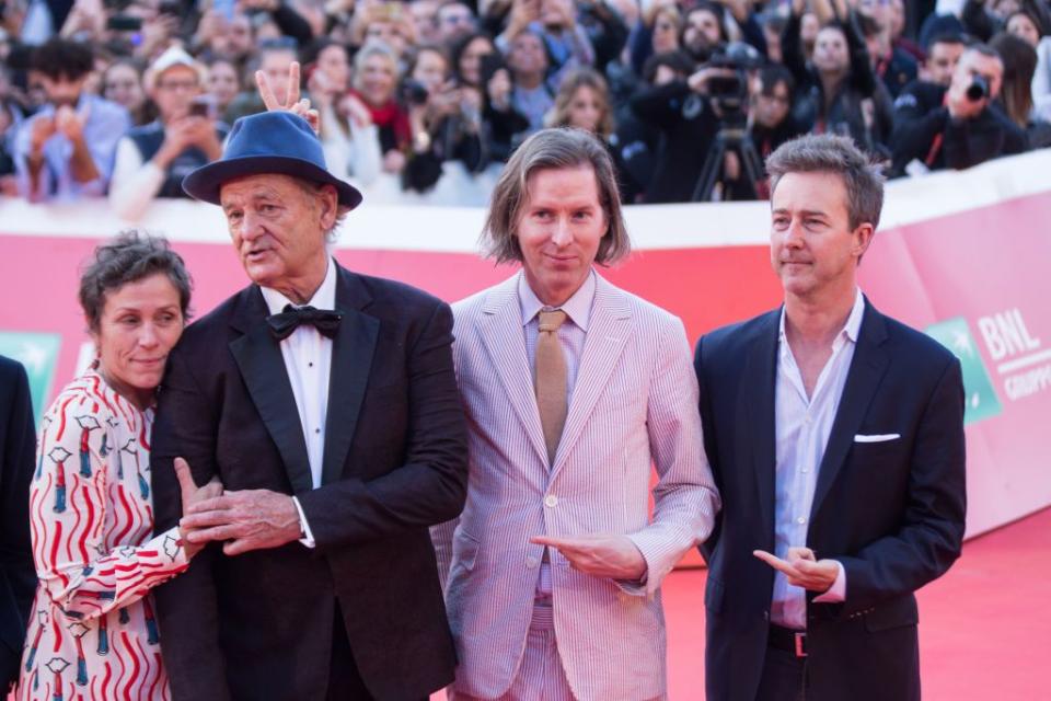 wes anderson, wearing a pink suit, and edward norton, wearing a black suit jacket and blue shirt