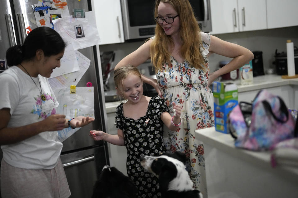 Sol, left, a 14-year-old from Argentina, and 8-year-old Maddie Hazelton joke around with some whipped cream as Sol's foster mother, Caroline Hazelton, and the family's two dogs look on, in Homestead, Fla., Monday, Dec. 18, 2023. Sol is among tens of thousands of children who have arrived in the United States without a parent during a huge surge in immigrants that's prompting congressional debate to change asylum laws. (AP Photo/Rebecca Blackwell)