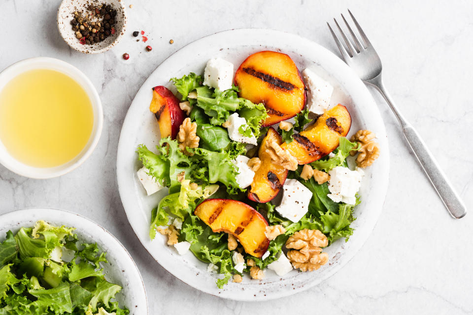 Summer salad with grilled peaches and feta cheese garnished with walnuts on a plate, top view. Healthy gourmet food