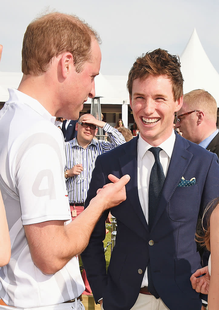 Prince William in a polo shirt chatting with Eddie Redmayne in a suit at an outdoor event