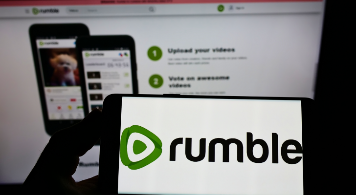 Person holding cellphone with logo of Canadian video platform company Rumble (RUM) Inc. on screen in front of business webpage. CFVI