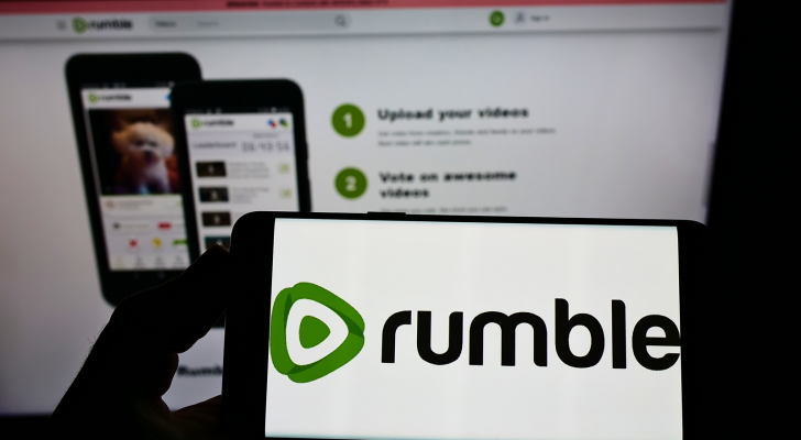 Person holding cellphone with logo of Canadian video platform company Rumble Inc. on screen in front of business webpage. CFVI 