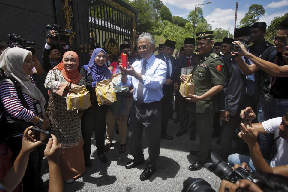 Malaysia's King Sultan Abdullah Sultan Ahmad Shah, center, hands out food parcels to the journalists who was camped outside the palace following the resignation of Prime Minister Mahathir Mohamad, in Kuala Lumpur, Tuesday, Feb. 25, 2020. After months of resisting pressure to hand over the premiership to his named successor, Mahathir Mohamad finally quit this week. But in a confounding twist, the 94-year-old leader emerged stronger than before, while his ruling alliance, which won a historic vote about two years ago, met its Waterloo. (AP Photo)