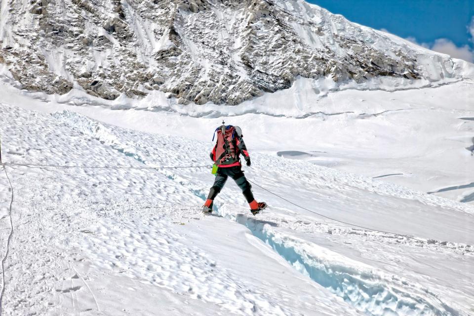 Climber jumping through a small crevasse along the snow-capped Khumbu Glacier on Mount Everest