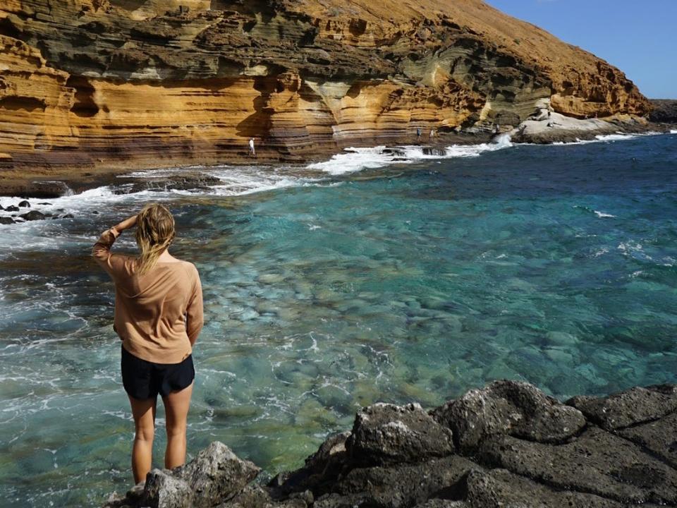 A woman wading into the ocean next to cliffs.