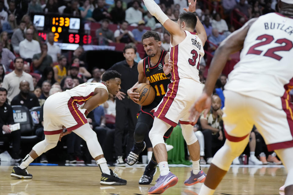 Atlanta Hawks guard Trae Young (11) works his way through the defense of Miami Heat guard Max Strus (31) and guard Kyle Lowry, left, during the first half of an NBA basketball play-in tournament game Tuesday, April 11, 2023, in Miami. (AP Photo/Rebecca Blackwell)