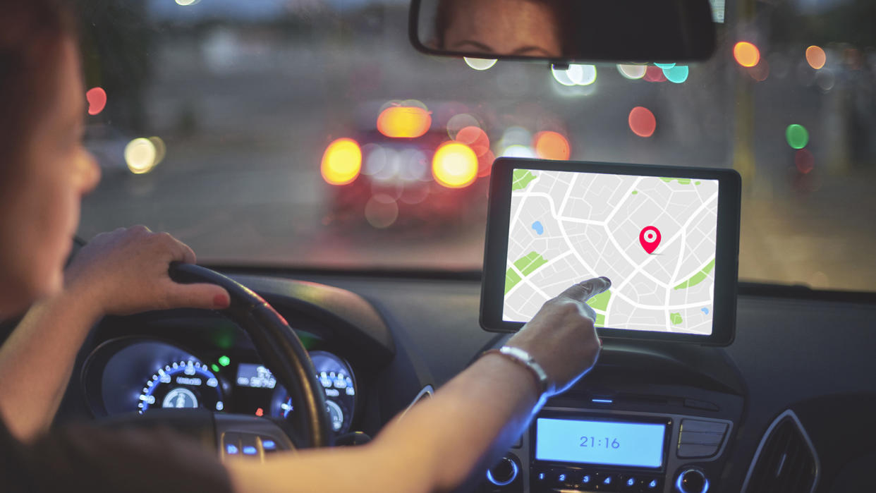 Rear view of woman driving car and touching screen of navigation system