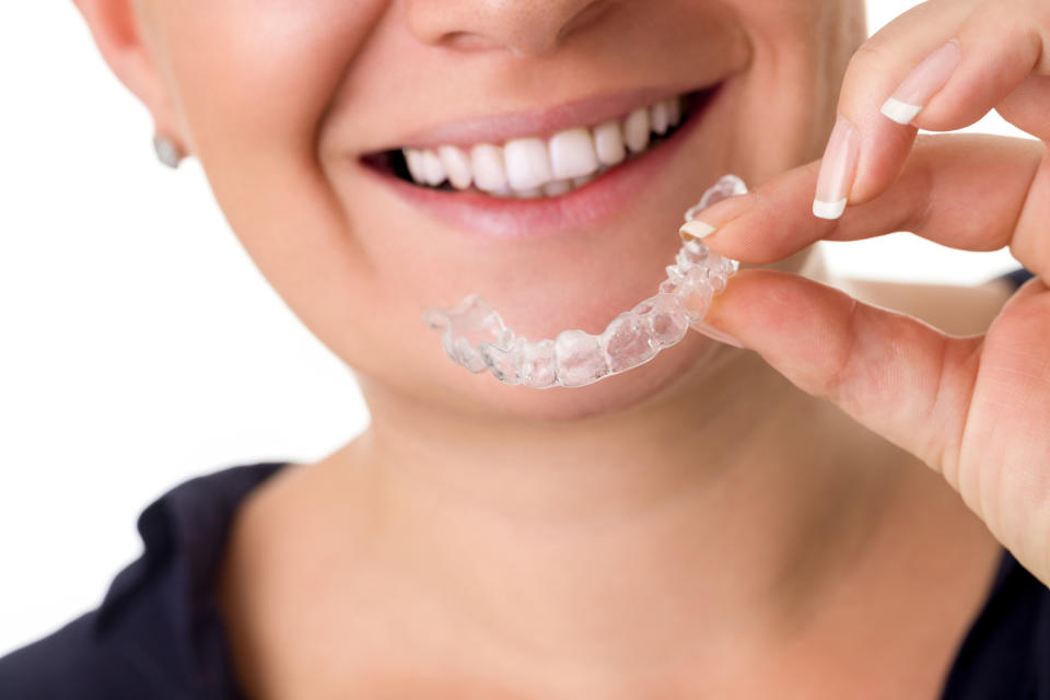 Smiling woman holding clear dental aligner