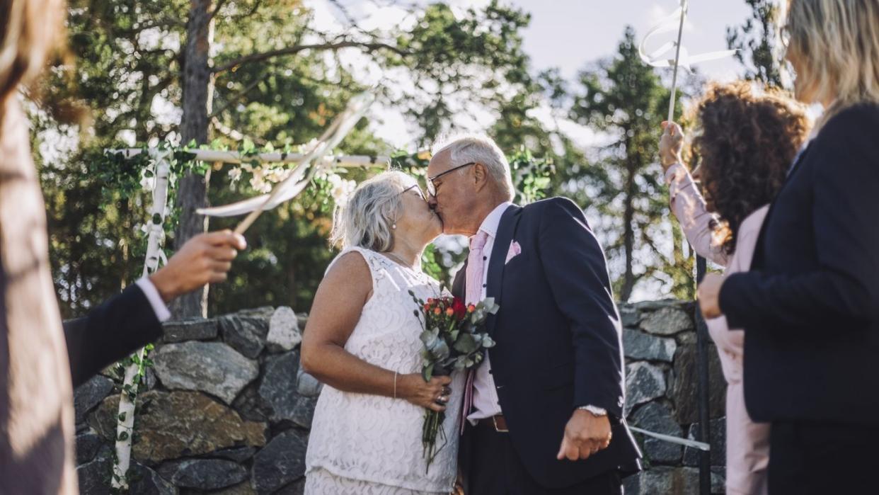 senior bride with bouquet kissing groom on mouth amidst guest during wedding celebration
