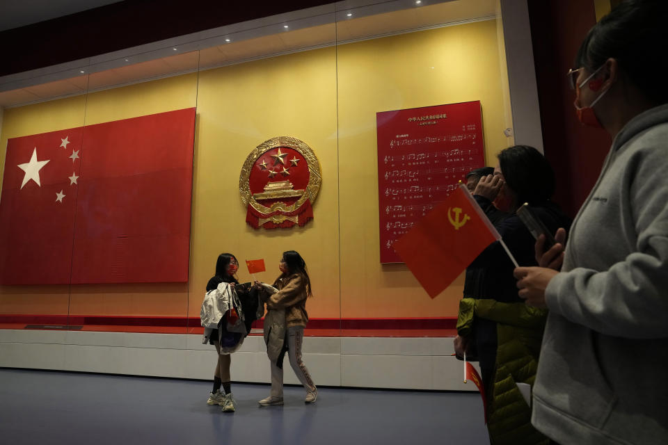 Visitors holding Communist Party flags past by the Chinese national flag, state emblem and score for the Chinese national anthem at the Museum of the Communist Party of China here in Beijing, China, Friday, Nov. 12, 2021. Chinese leader Xi Jinping emerges from a party conclave this week not only more firmly ensconced in power than ever, but also with a stronger ideological and theoretical grasp on the ruling Communist Party's past, present and future. (AP Photo/Ng Han Guan)