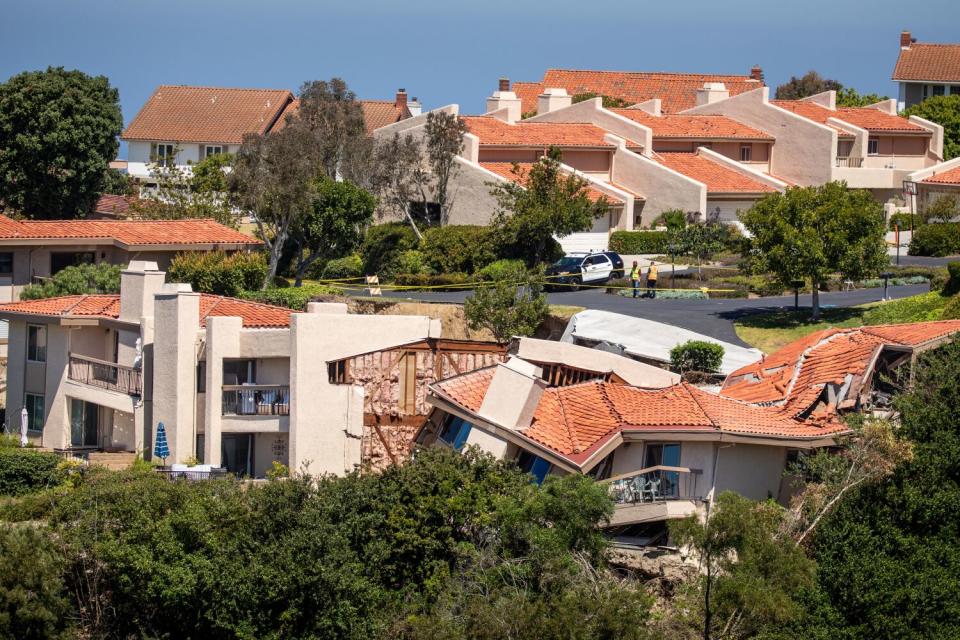 A view of homes along a road, some with broken roofs and tilting