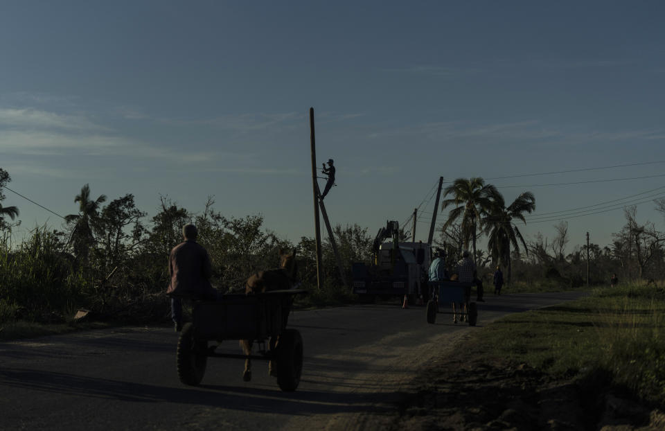 A worker repairs power lines downed by Hurricane Ian along a road where people travel by horse-drawn carts in La Coloma, in the province of Pinar del Rio, Cuba, Wednesday, Oct. 5, 2022. (AP Photo/Ramon Espinosa)