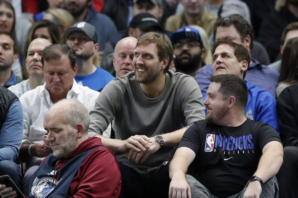 Former player Dirk Nowitzki, center, and team owner Mark Cuban, right, watch play between the Cleveland Cavaliers and Dallas Mavericks in the second half of an NBA basketball game in Dallas, Friday, Nov. 22, 2019. (AP Photo/Tony Gutierrez)