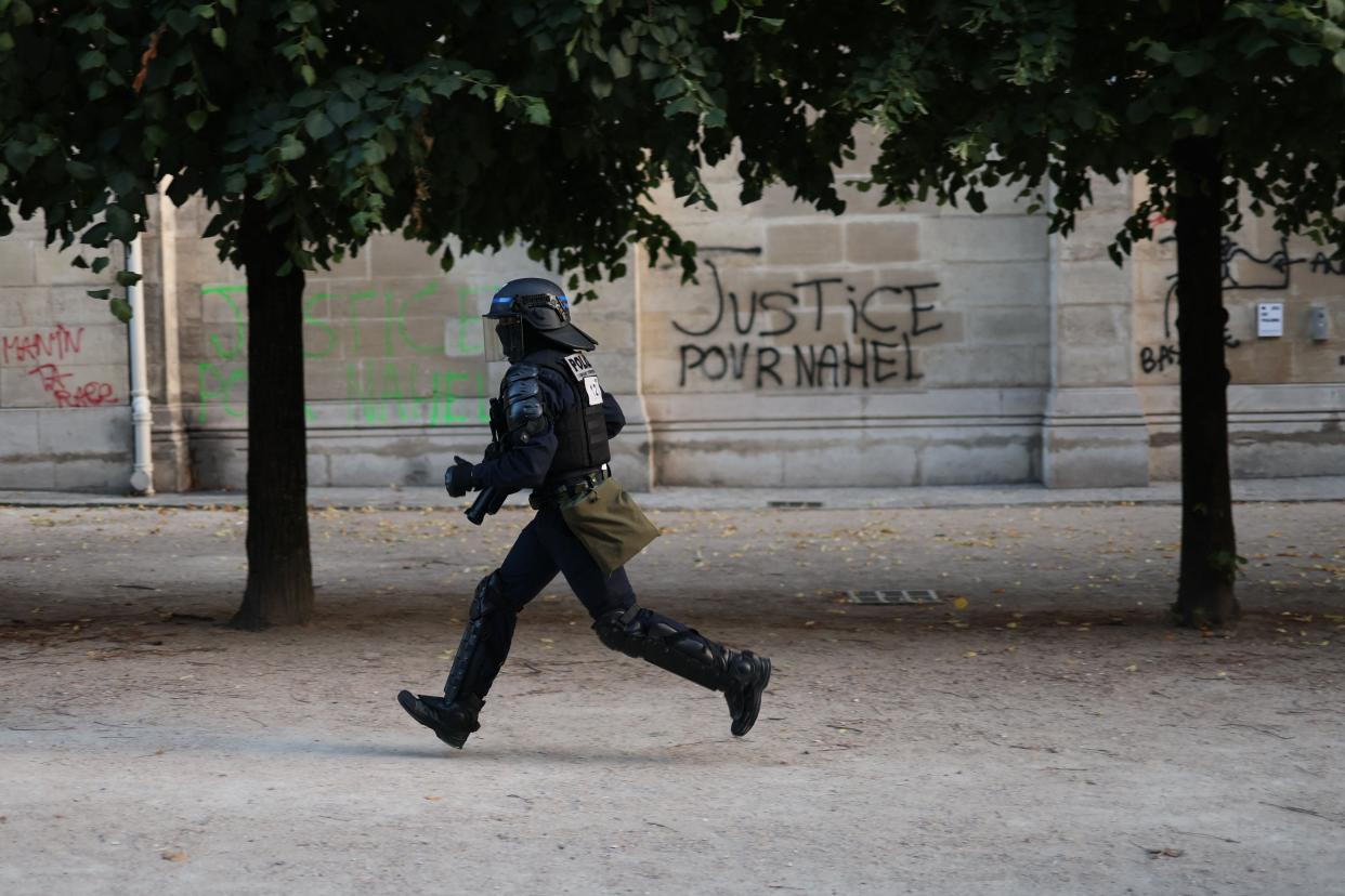 A CRS riot police officer runs past graffiti reading 