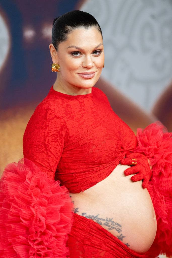 A closeup of jessie j with her hand on her exposed pregnant belly at an event