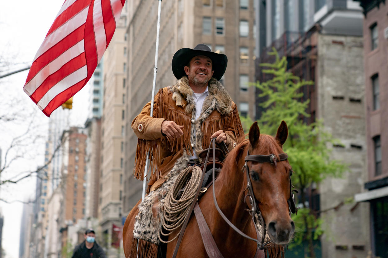 Couy Griffin holds an American flag as he rides his horse along a New York street.