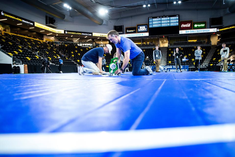 Josh Schamberger and Luke Eustice tape down lines while setting up mats before the finals of the Dan Gable Donnybrook high school girls wrestling tournament earlier in December.