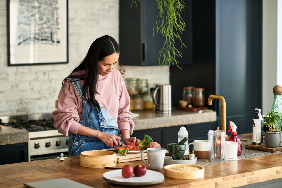 mid adult woman chopping ingredients for meal, standing behind kitchen worktop