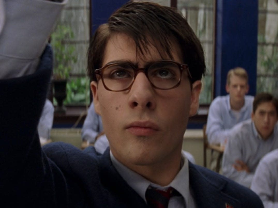 jason schwartzman, as a teenager, playing max in rushmore. he's wearing a suit and glasses, seen from the front writing on a blackboard and looking upward