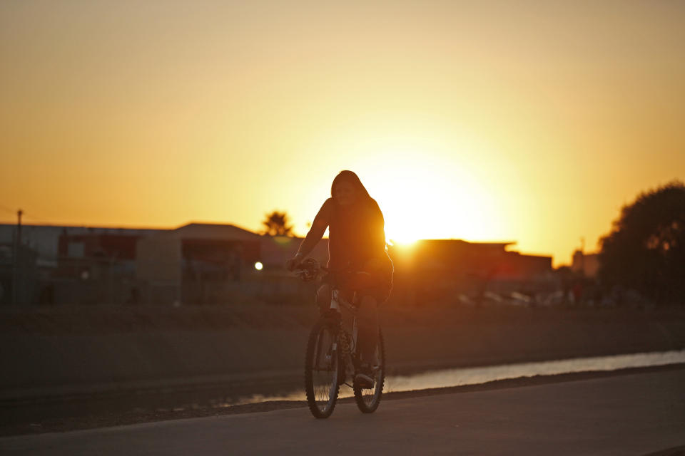 A woman rides her bicycle next to the Grand Canal as a very hot day ends in Phoenix on July 6, 2023.  (Dario Lopez-Mills / AP)