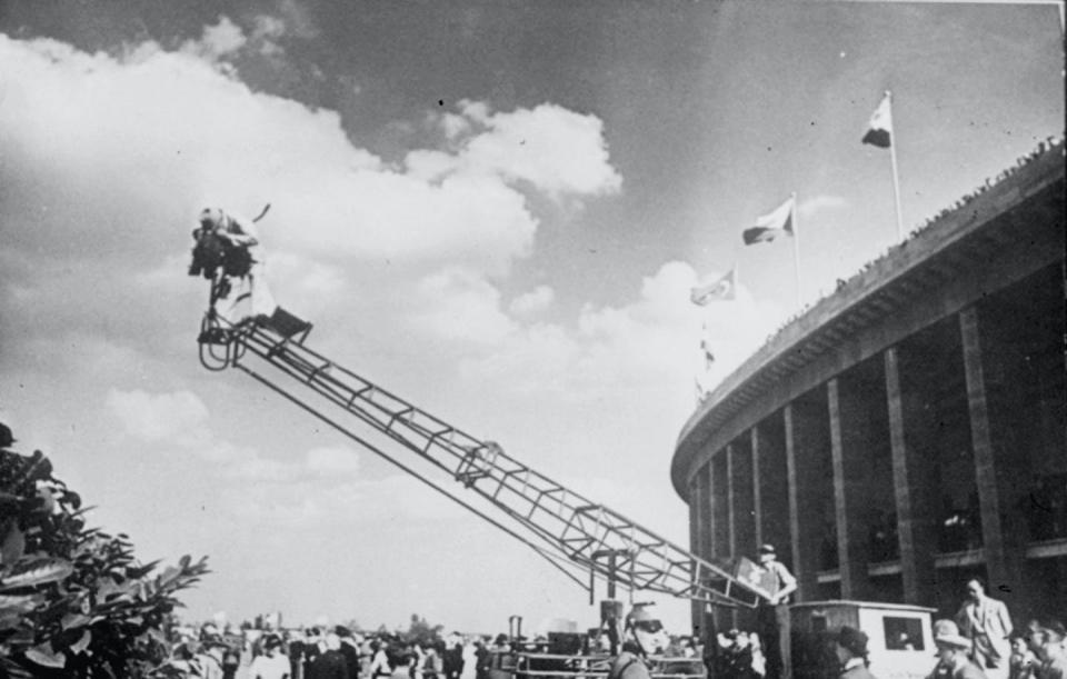 A black and white image of a cameraman on a crane above a crowd