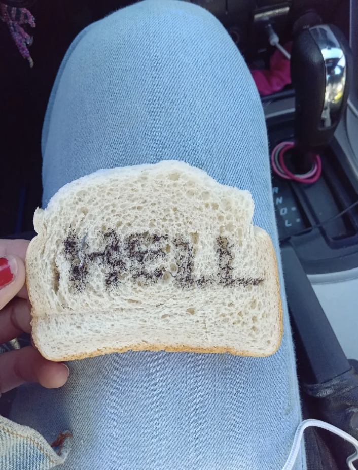 Someone holding a slice of bread with "HELL" written on it