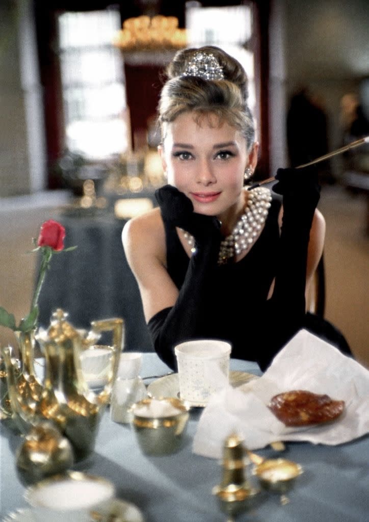 Audrey Hepburn in "Breakfast at Tiffany's", wearing a black dress, tiara, and gloves, with a cigarette holder