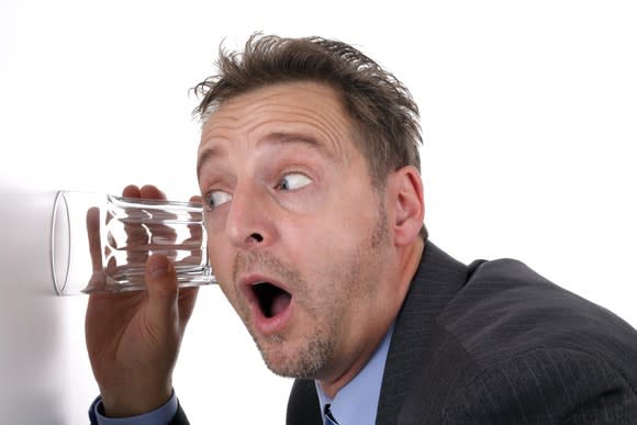 A man in a suit listens through a wall using a glass.