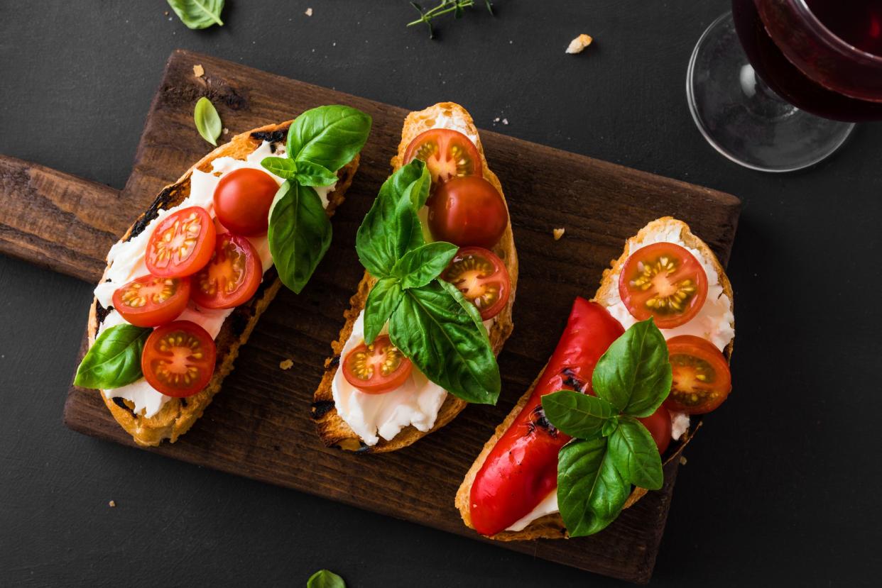 Bruschetta sandwiches with tomatoes, cream cheese, grilled paprika and basil on wooden board, close up. Traditional italian snack for wine - grilled bruschetta toasts.