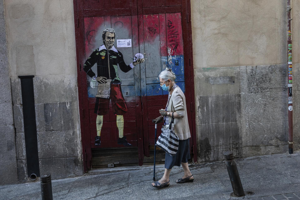 An elderly woman wearing a face mask to protect against the coronavirus walks past a painting named "to be or not to be" by artist TVBOY and depicting Spanish government's top virus expert Fernando Simon in Madrid, Spain, Sunday, Sept. 13, 2020. (AP Photo/Bernat Armangue)