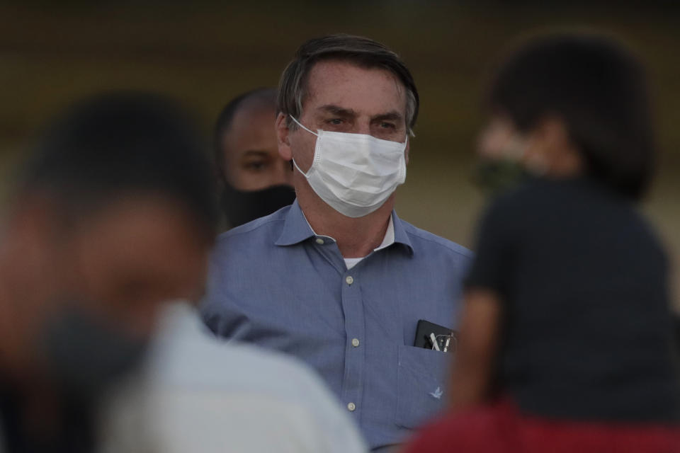 Brazil's President Jair Bolsonaro, who is infected with COVID-19, wears a protective face mask as he stands with supporters during a Brazilian flag retreat ceremony outside his official residence the Alvorada Palace, in Brasilia, Brazil, Friday, July 24, 2020. Bolsonaro has tested positive for the new coronavirus for the third time, following his July 7 announcement that he had COVID-19, the Brazilian government confirmed. (AP Photo/Eraldo Peres)