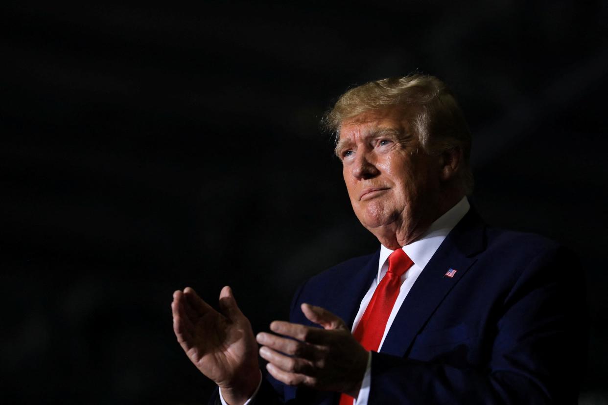 donald trump in red tie and suit claps while half smiling