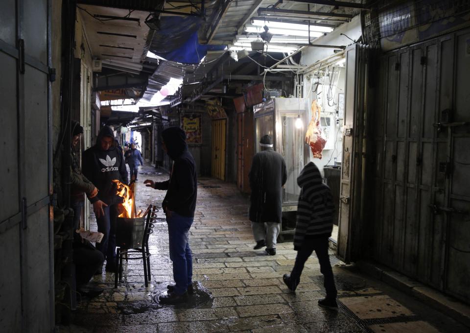 People warm themselves near a fire in a market in Jerusalem's Old City December 12, 2013. Schools and offices in Jerusalem and parts of the occupied West Bank were widely closed and public transport paused after heavy snowfall on Thursday. REUTERS/Darren Whiteside (JERUSALEM - Tags: ENVIRONMENT)