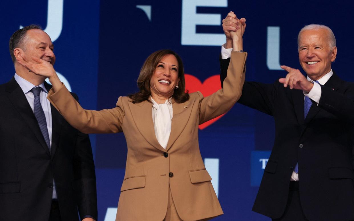 Biden and Harris smile as they raise their arms on stage