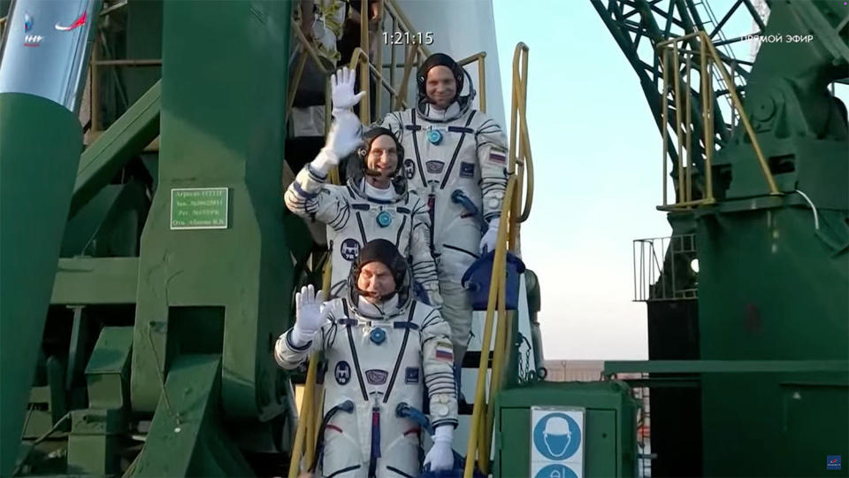 Soyuz commander Aleksey Ovchinin, bottom, NASA Don Pettit, center, and cosmonaut Ivan Vagner, top, wave to supporters at the bottom of their Soyuz rocket before they take an elevator to the top of the bridge to strap in for launch. (NASA) / Credit: NASA/Roscosmos