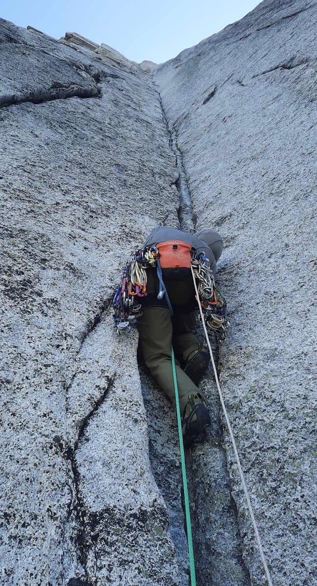 Man climbs vertical granite corner with climbing gear hanging from his harness.