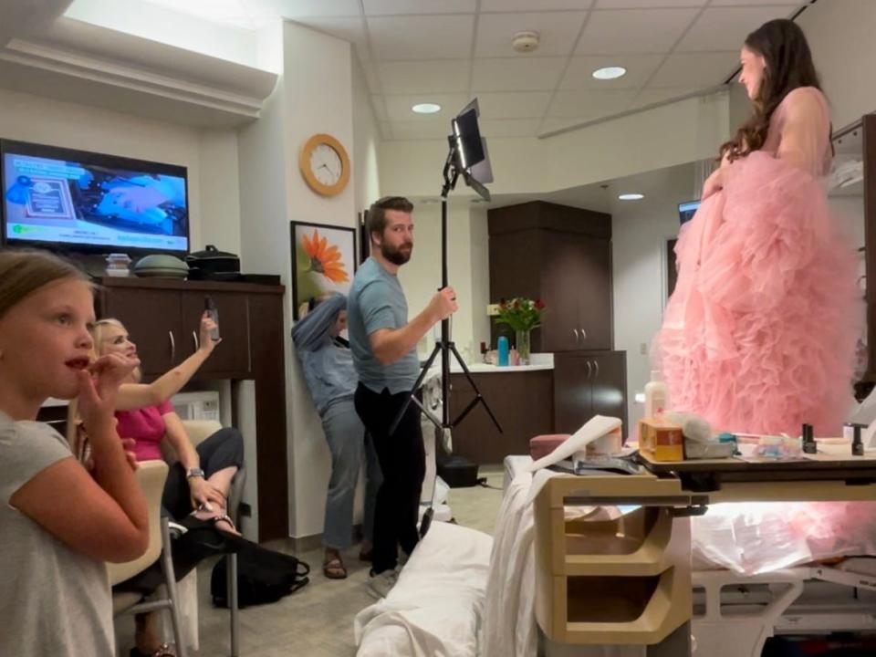 Jackie Kunzelman, wearing a flowing pink dress, poses for a maternity photoshoot on top of her hospital bed.