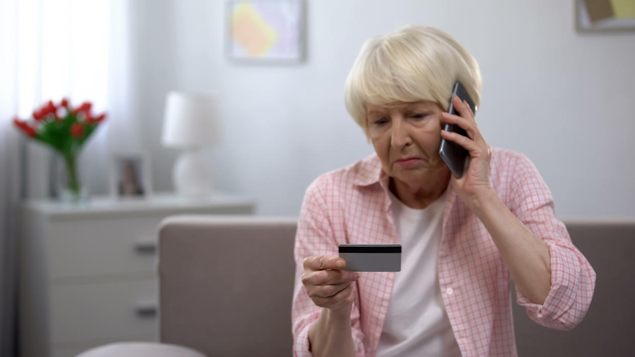 Elderly woman looking concerned while on the phone, looking at her credit card.