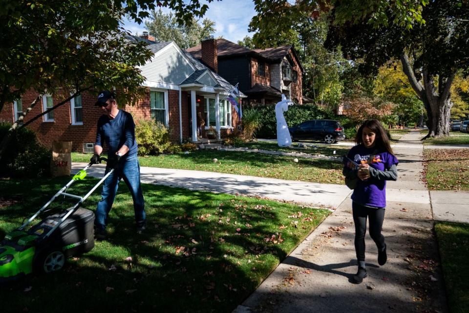 Michelle Bortnick walks down a sidewalk next to a man mowing a lawn.