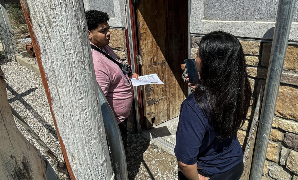 During a home visit, Julia Madera, an attendance advocates from Northridge High School, talks by phone with the mother of a student who hasn’t shown up to school, as another advocate, Domanic Castillo, looks on. (Ann Schimke/Chalkbeat)