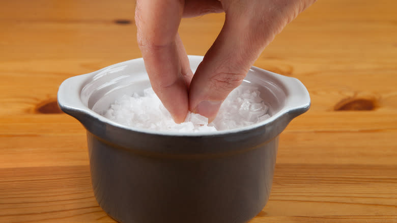 Fingers pinching salt from pot