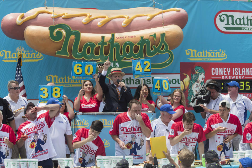 <p>Mater of Ceremony George Shea, top center, announces that reigning champion Joey Chestnut, bottom center, is winning the men’s competition of the Nathan’s Famous Fourth of July hot dog eating contest in the final seconds of the competition, Wednesday, July 4, 2018, in New York’s Coney Island. Defending champion Joey Chestnut broke his own world record by eating 74 hot dogs in 10 minutes. (Photo: Mary Altaffer/AP) </p>