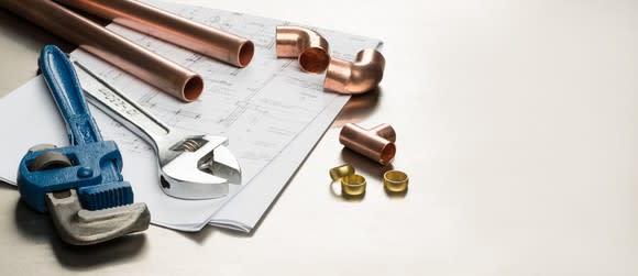 Wrenches, copper pipes, and pipe fittings atop a set of plans.