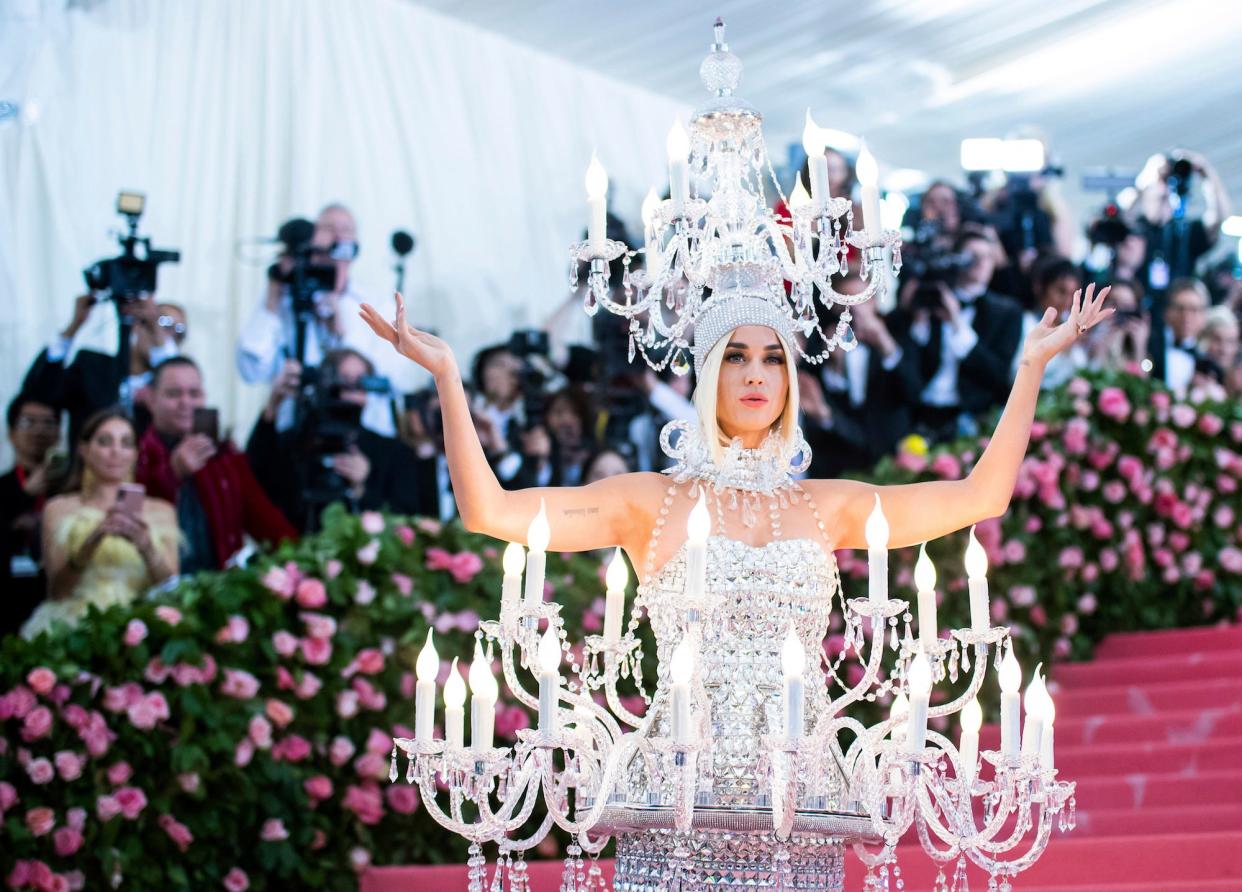Katy Perry on the red carpet, wearing a dress and headpiece shaped like a chandelier.