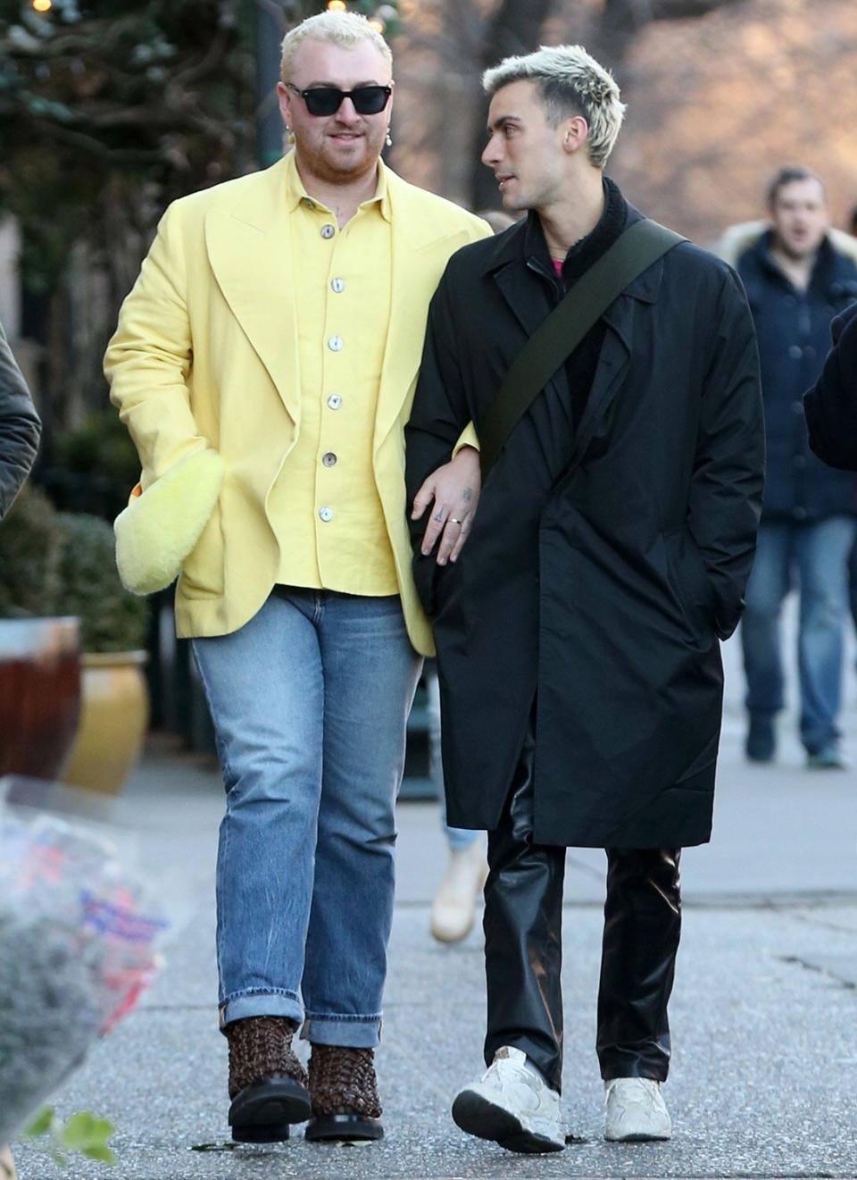 Singer Sam Smith sports a yellow jacket, rolled-up jeans and Bottega Veneta lug boots as they kiss a male friend while locking arms in Soho in New York City.