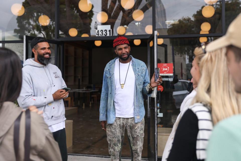 Two men stand in front of a small audience outside a cafe in Leimert Park.